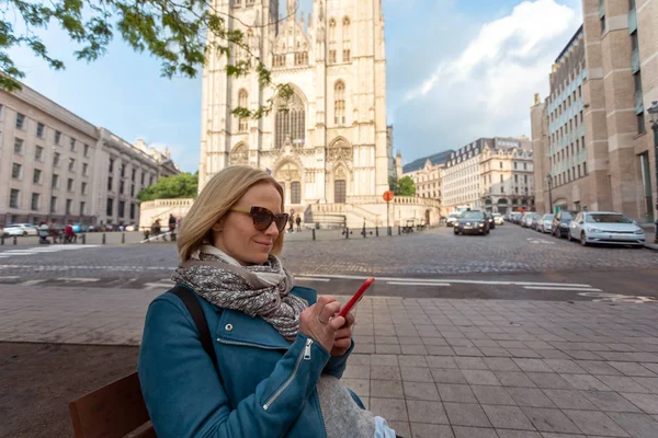 比利时布鲁塞尔圣米歇尔和古杜拉大教堂的背景下，坐在街上拿着电话的妇女 — 图库照片