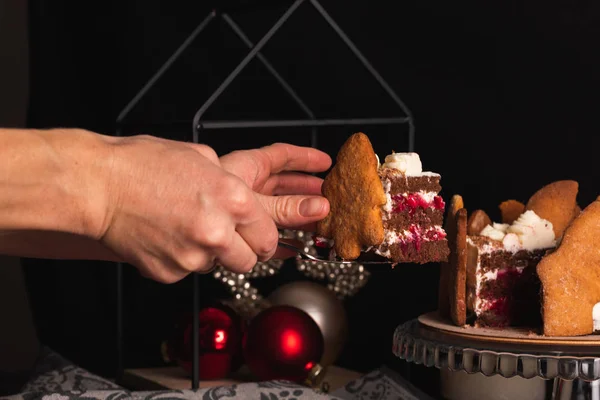 Female hands cut a piece of cake Black Forest decorated in Christmas style.