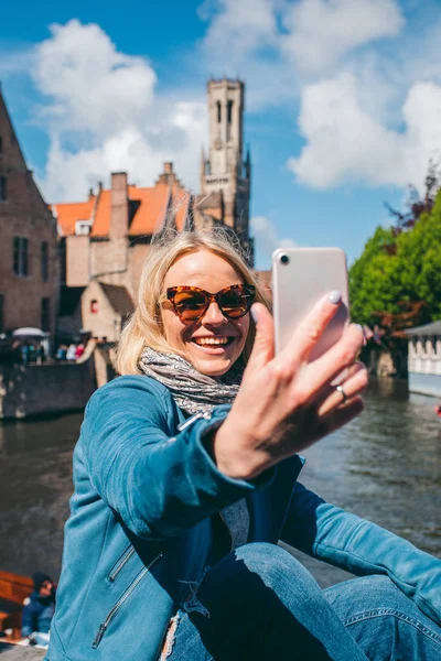 Όμορφη νεαρή κοπέλα παίρνει selfie φωτογραφία στο φόντο του διάσημου τουριστικού προορισμού με ένα κανάλι στην Bruges, Βέλγιο — Φωτογραφία Αρχείου
