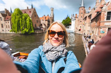 Güzel genç bir kız, Belçika 'nın Bruges kentindeki ünlü turist merkezinin arka planında selfie çekiyor.