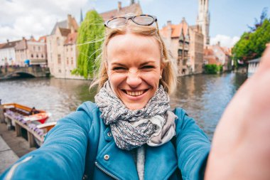 Güzel genç bir kız, Belçika 'nın Bruges kentindeki ünlü turist merkezinin arka planında selfie çekiyor.