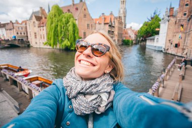 Güzel genç bir kız, Belçika 'nın Bruges kentindeki ünlü turist merkezinin arka planında selfie çekiyor.
