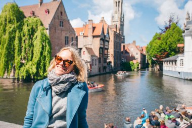 Belçika, Bruges 'de bir kanalı olan ünlü bir turist bölgesinin arka planında güzel bir genç kız oturuyor.