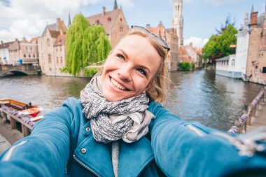 Güzel genç bir kız, Belçika 'nın Bruges kentindeki ünlü turist merkezinin arka planında selfie çekiyor.