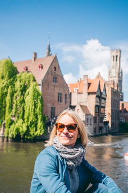 Belçika, Bruges 'de bir kanalı olan ünlü bir turist bölgesinin arka planında güzel bir genç kız oturuyor.