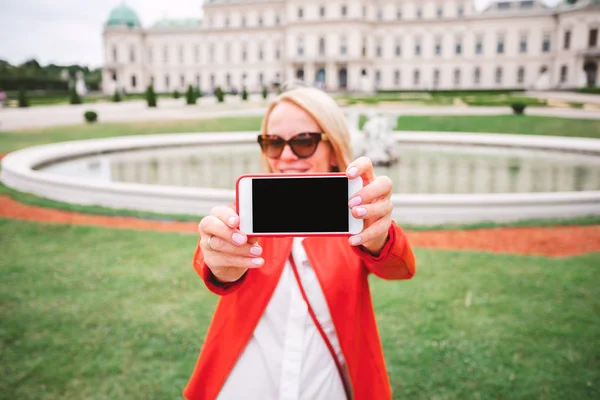 在奥地利维也纳的贝尔韦代雷宫建筑群的公园里，一个小女孩正在给人看她手机的屏幕 — 图库照片