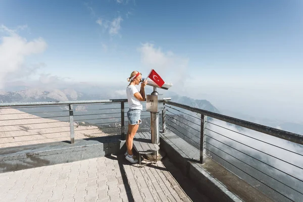 La giovane turista si trova su una piattaforma panoramica del monte Tahtali a Kemer con una bandiera rossa della Turchia e guarda in binocolo, Turchia — Foto Stock
