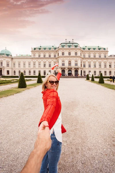 一位拿着奥地利国旗的年轻女子手牵着丈夫的手，与奥地利维也纳的一座宫殿相对立 — 图库照片