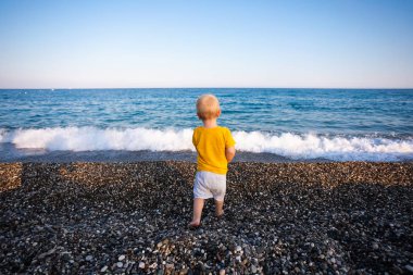 Küçük çocuk denize taş ve çakıl atıyor..