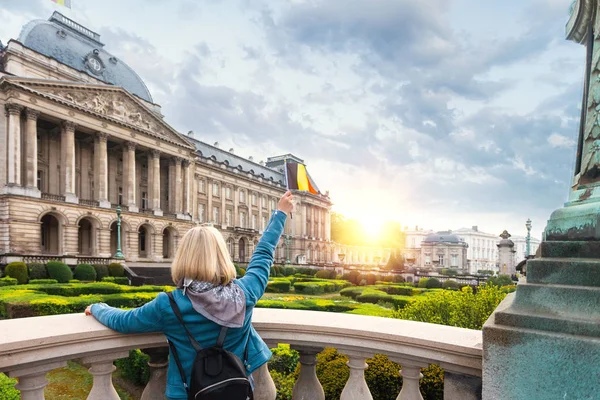 Mujer turista de pie con su espalda a la cámara y ondeando la bandera de Bélgica contra el fondo del Palacio Real en Bruselas — Foto de Stock