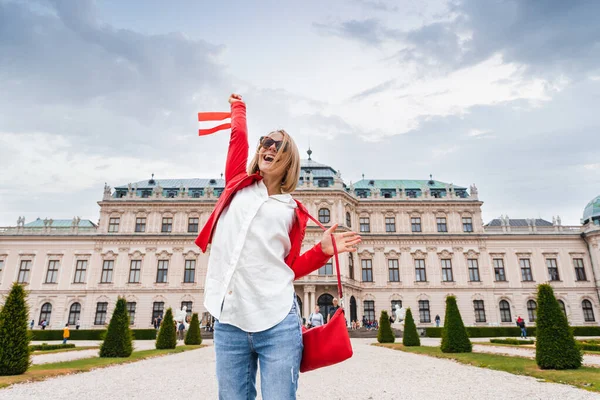 Viajero femenino con la bandera de Austria con el telón de fondo del Palacio del Belvedere Superior en Viena . — Foto de Stock