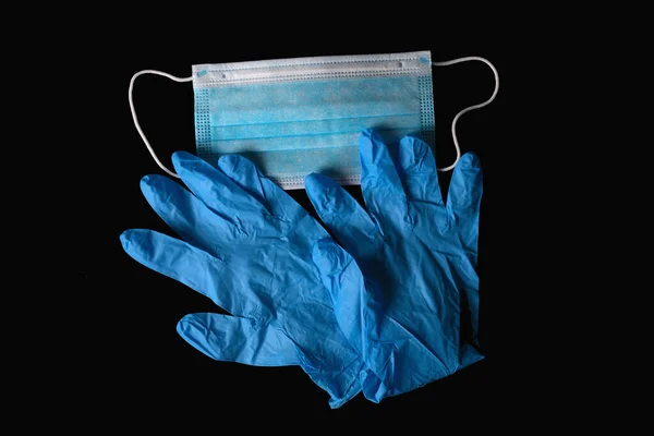 黒い背景に隔離された青い医療用滅菌マスクと青い滅菌手袋. — ストック写真