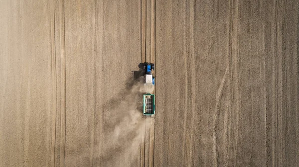 Vue aérienne d'un tracteur bleu travaillant dans un champ avec un engrais et un épandeur de semences — Photo