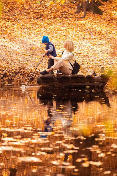 Feliz jovem mãe e seu filho passar o tempo no parque de outono perto da lagoa. — Fotografia de Stock