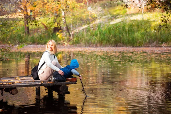 Feliz jovem mãe e seu filho passar o tempo no parque de outono perto da lagoa. — Fotografia de Stock