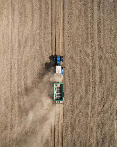Вид с воздуха на голубой трактор, работающий в поле с удобрением и семеноразбрасывателем — стоковое фото