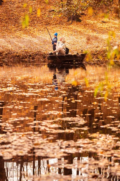 Happy young mother and her son spending time in the autumn park near the pond.