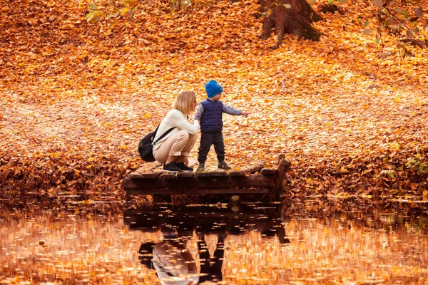 Šťastná mladá matka a její syn tráví čas v podzimním parku u rybníka. — Stock fotografie