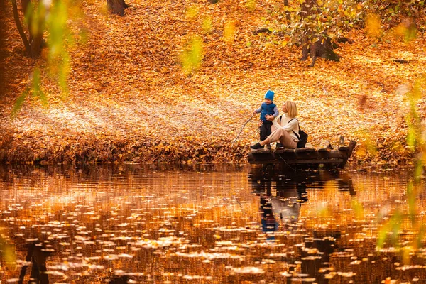 Gelukkig jong moeder en haar zoon tijd doorbrengen in de herfst park in de buurt van de vijver. — Stockfoto