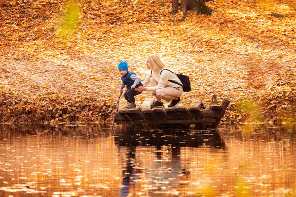 Happy young mother and her son spending time in the autumn park near the pond.