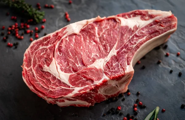 Raw cowboy steak with seasonings on stone background, prime rib — Stock Photo, Image