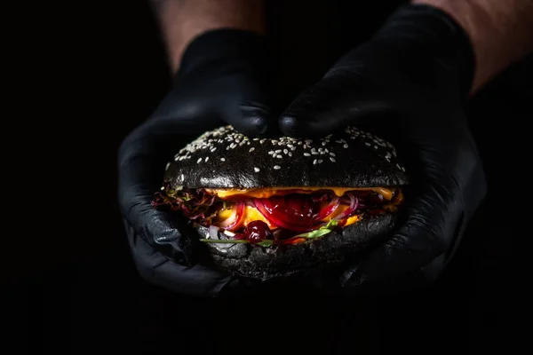 Primer plano de las manos sosteniendo hamburguesa negra jugosa con sauc de arándano — Foto de Stock