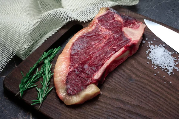 Sucho zrající Striploin steak a sůl na tmavé dřevěné desce, rustikální s — Stock fotografie