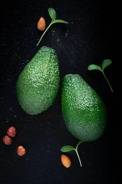 Twee avocado 's op een zwarte stenen achtergrond met bladeren en noten. — Stockfoto