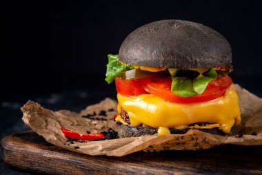 Kraft kağıdında peynirli ve domatesli bir siyah burger. Tahtada siyah ekmekli çizburger.