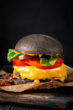 Kraft kağıdında peynirli ve domatesli bir siyah burger. Tahta tahtada siyah ekmekli çizburger. Yaklaş.