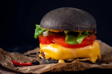 Koyu arkaplanda Kraft kağıdında peynirli ve domatesli bir siyah burger.