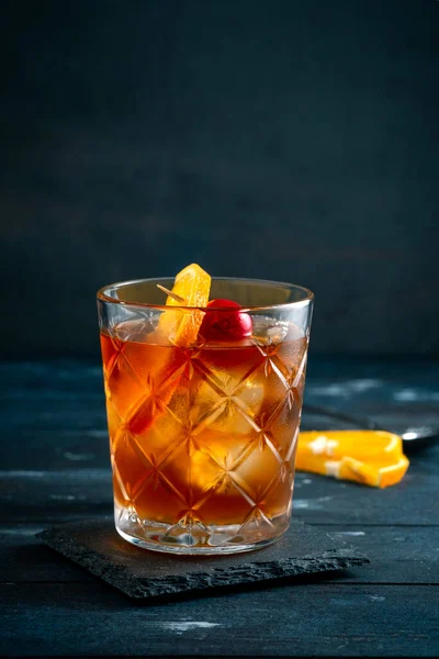 Whiskey sour cocktail with a slice of orange, cherry and ice, a classic alcoholic drink on dark background
