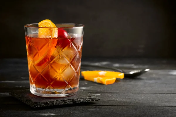 Whiskey sour cocktail with a slice of orange, cherry and ice, a classic alcoholic drink on black background