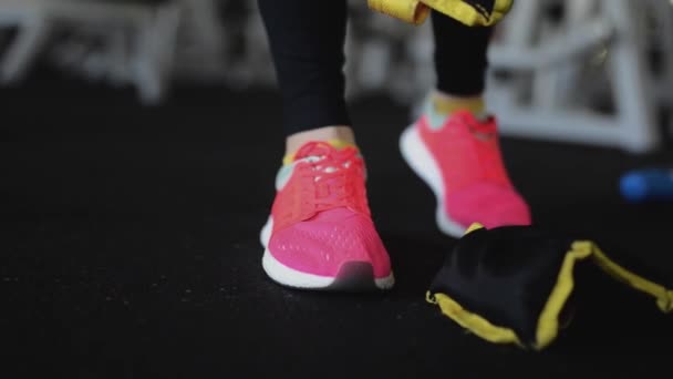 Close-up mulher em fitness rosa sapatos vestido pesos. Exercício no ginásio ou em casa, alongamento, detalhe de belas pernas pulando. Esportista esticando em tênis . — Vídeo de Stock