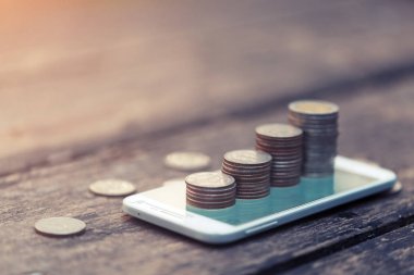 cep telefonu online iş ve yatırım kavramı için ahşap arka plan üzerinde para yığınları.