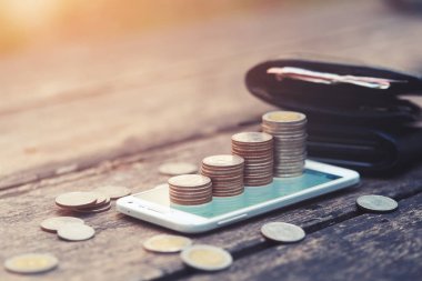 cep telefonu online iş ve yatırım kavramı için ahşap arka plan üzerinde para yığınları.