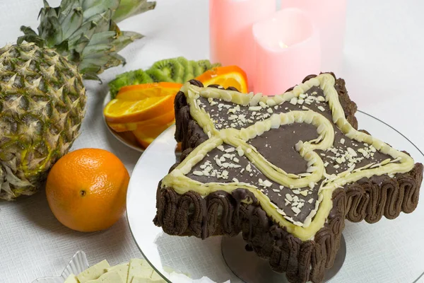 Dessert for a loved one vegan for the holiday. Angle view. Star-shaped chocolate cake with a heart in on a white background. Candles, pineapple, slices of orange and kiwi, tofu cheese on a saucer