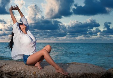 Güzel genç esmer kadın bir kayaya okyanus tarafından germe