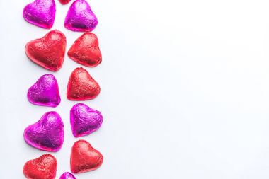 Beyaz arka plan sol tarafında kırmızı ve pembe folyo sarılı çikolata Sevgililer günü kalpleri