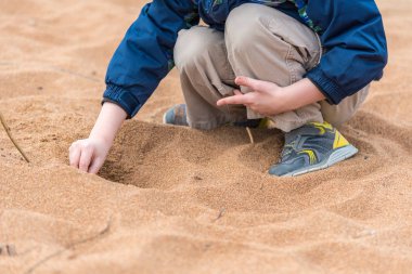 Okul öncesi yaş çocuk kuma oturur ve bir delik elleriyle kazıyor
