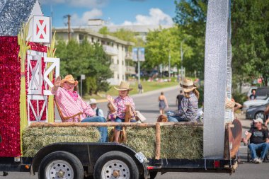 Williams Lake, British Columbia/Canada - July 2, 2016: people in western dress wave to the crowds from their farm themed parade float at the annual Stampede Parade in downtown Williams Lake. clipart