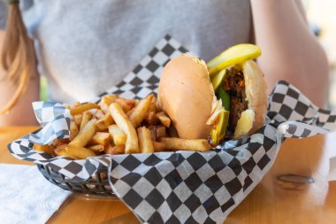 Açık veranda masasında elinde vejetaryen siyah fasulye burgeri ve patates kızartması olan sepetin yakın çekimi.