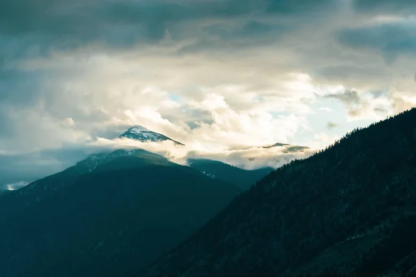 Schneebedeckter Berggipfel Umgeben Von Dramatischen Wolken Und Nebel Mit Sonnenlicht — Stockfoto