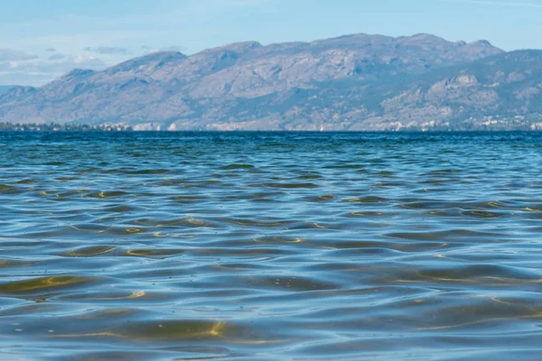 Close-up of gentle waves on Okanagan Lake with view of mountain and blue sky