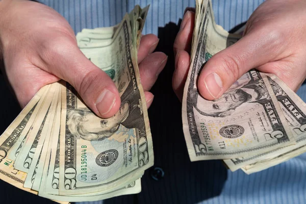 Man's hands holding out piles of cash in American five and twenty dollar bills