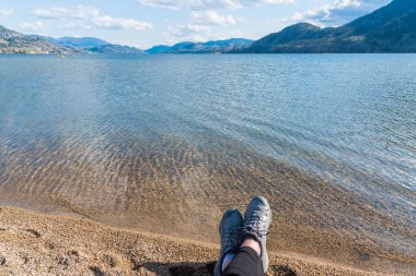 Kumsalda dinlenen kadın Skaha Gölü, dağlar ve mavi gökyüzü manzaralı