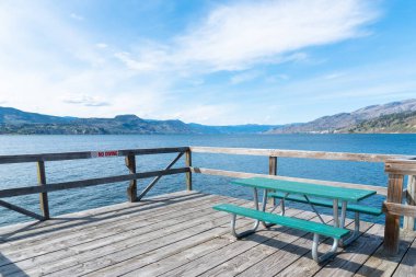 Naramata Rıhtımı 'nda piknik masası Okanagan Gölü, dağlar ve mavi gökyüzü manzaralı.
