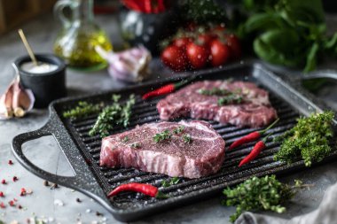 Çiğ taze et. Baharatlar, sebzeler ve otlar ile, bir ızgara tavada malzemelerle iki biftek