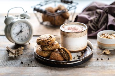 Ev yapımı fındıklı kurabiyeler ve ahşap bir masada seramik bir fincanda kahve. Kahve içme zamanı. Arka planda çalar saat var. Kahvaltı.