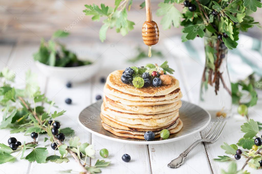 Pancakes with fresh berries of raspberries, currants, blueberries, with honey and tea